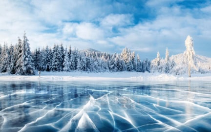 Cracks on the surface of the blue ice. Frozen lake in winter mountains. It is snowing. The hills of pines. Carpathian Ukraine Europe.