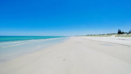 Drone aerial view of wide open white sandy beach, taken at Tennyson, South Australia with nearby luxury two story homes overlooking the coast.
